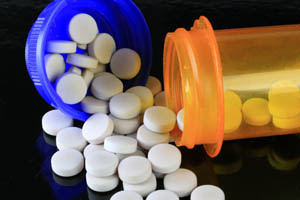 White tablets spilled from blue and orange prescription bottles onto a dark surface.