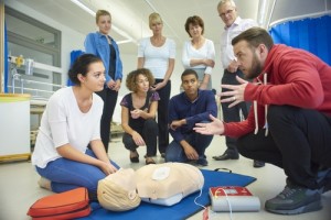 Person performing CPR chest compressions on a training manikin with an automated external defibrillator (AED) in use during a first aid training session.
