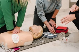 Person performing CPR chest compressions on a training manikin with an automated external defibrillator (AED) in use during a first aid training session.