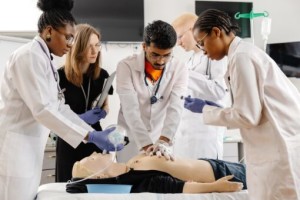 Person performing CPR chest compressions on a training manikin with an automated external defibrillator (AED) in use during a first aid training session.