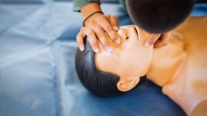Person performing CPR chest compressions on a training manikin with an automated external defibrillator (AED) in use during a first aid training session.