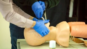 Person performing CPR chest compressions on a training manikin with an automated external defibrillator (AED) in use during a first aid training session.