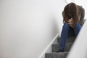 A person sitting on stairs with head bowed and hands clasped, appearing upset or distressed.