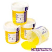 Four plastic containers resembling urine specimen cups, filled with yellow liquid and labeled with white stickers, with one cup tipped over and liquid spilling out.