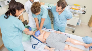 Medical professionals practicing CPR on a training mannequin in a clinical simulation setting.