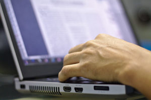 Close-up of a hand typing on a laptop keyboard with a blurry document visible on the laptop screen.