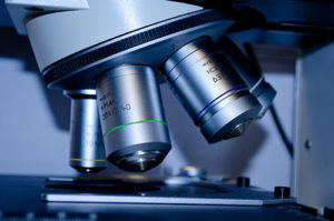 Close-up view of a microscope with three objective lenses, focused on a glass slide for scientific observation and research.