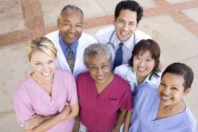 Group of smiling healthcare professionals standing together outdoors, looking up at the camera.