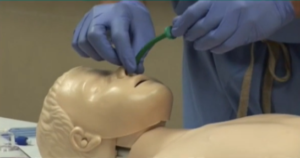Healthcare professional practices inserting a nasal airway tube into a pediatric mannequin, demonstrating a medical procedure for airway management or training purposes.