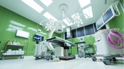 Modern hospital operating room with green tiled walls, surgical lights, medical monitors, and advanced medical equipment arranged around an empty operating table.
