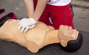 Person practicing CPR chest compressions on a medical training mannequin outdoors.