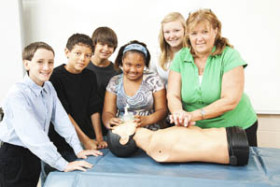 Group of students and a teacher practicing CPR on a training mannequin in a classroom setting.