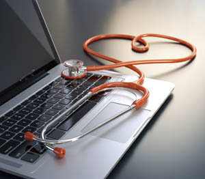 A stethoscope with orange tubing is resting on a laptop keyboard, with part of the tubing arranged in the shape of a heart.