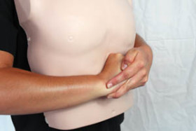 Person demonstrating the Heimlich maneuver on a CPR training manikin, with hands positioned just above the abdomen.