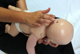 Person demonstrating infant choking first aid by giving back blows to a baby mannequin.