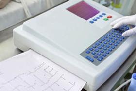 Gloved hand operating an electrocardiogram (ECG) machine with printed heart rate data visible on paper.