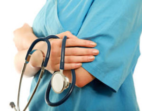 Medical professional in blue scrubs holding a stethoscope with arms crossed.