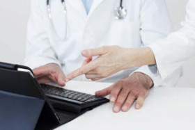 Two doctors in white coats discussing information while using a tablet and keyboard in a medical office.