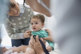 Doctor examining baby with a stethoscope while the mother smiles and gently holds the child during a medical checkup in a clinic.