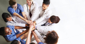 Group of diverse healthcare professionals standing in a circle, stacking their hands together in a show of teamwork and unity.