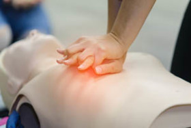 Hands performing chest compressions on a CPR training mannequin.