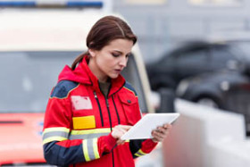 Female emergency responder in a red uniform using a digital tablet, standing outdoors near a response vehicle.