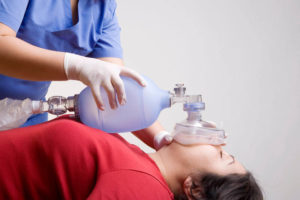 Medical professional uses a manual resuscitator to assist breathing for a patient lying on their back.