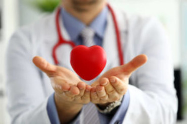 Doctor holding hands out with a red heart model hovering above palms, symbolizing healthcare and heart health.
