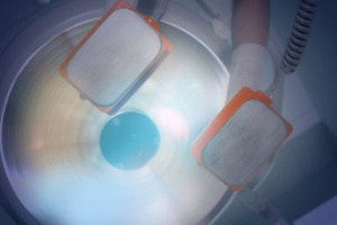 Medical professional holding defibrillator paddles above a patient, preparing to deliver an electric shock for emergency cardiac resuscitation.