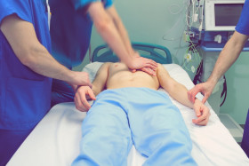 Medical team performing CPR chest compressions on a patient lying on a hospital bed in an emergency room setting.