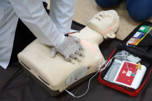 Person performing CPR chest compressions on a training manikin with an automated external defibrillator (AED) in use during a first aid training session.
