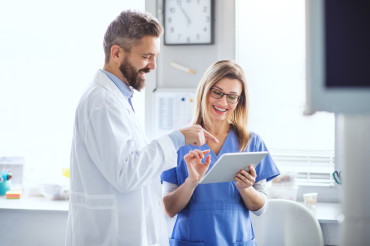 Male doctor and female nurse smiling and reviewing information on a digital tablet in a bright medical office.