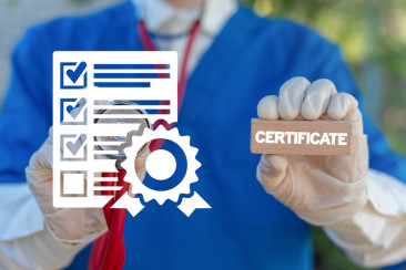  a man in blue scrubs holds wearing a stethoscope holds a wooden block that spelled certificate