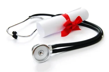 A stethoscope is on a table with a rolled paper tied with a red ribbon that signifies ACLS certificate