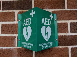 Green AED training sign mounted on a brick wall, indicating the location of an Automated External Defibrillator
