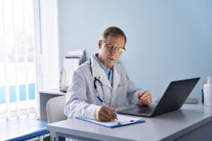 doctor-wearing-eye-glasses-infront-of-laptop-and-holding-a-pen