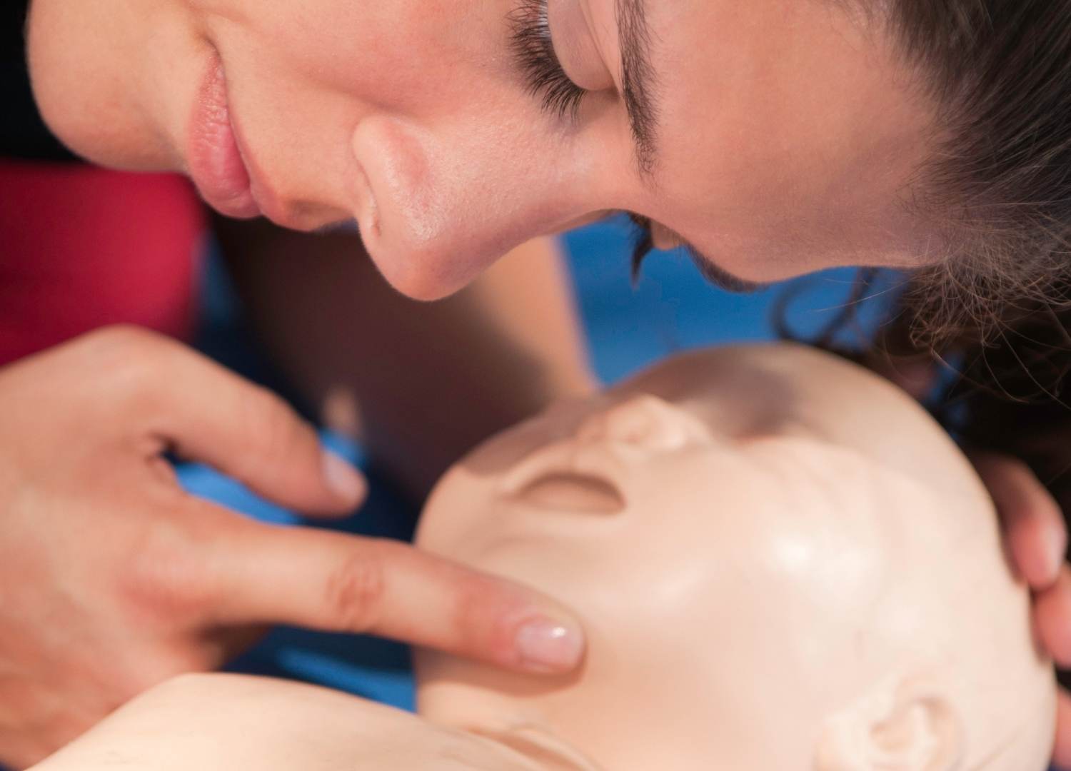 Healthcare professional checking an infant mannequin's pulse during CPR training.