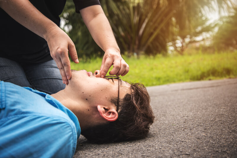 unconscious man lying on the ground and a rescuer doing head tit chin lift maneuver