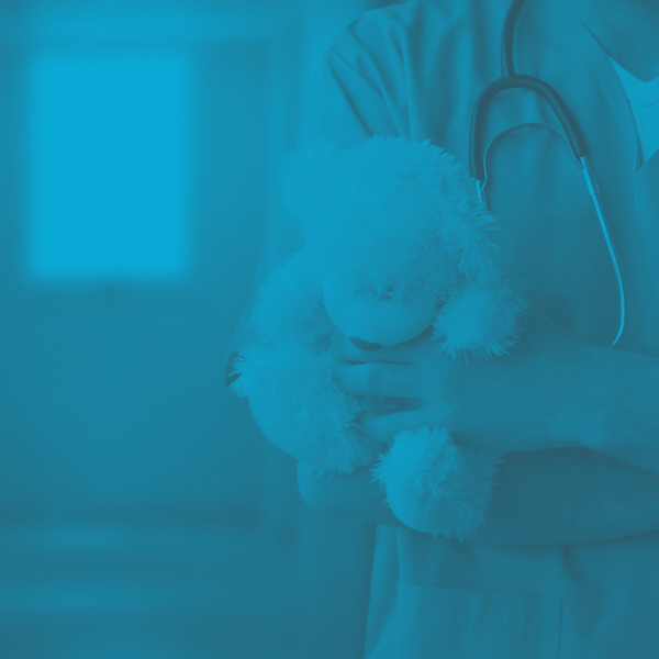PALS certified healthcare staff stands on a hopsital corridor and is holding a teddy bear
