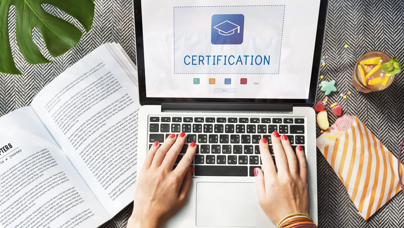 a newly certified medical professional who took a PALS certification is in front of a laptop displaying a graduation cap on the screen