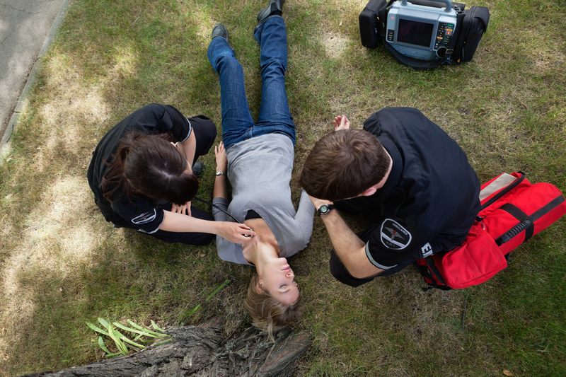 Two medical personnel kneel to help a woman lying on the grass.